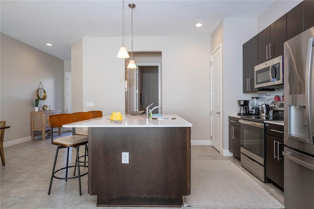 kitchen with appliances with stainless steel finishes, a breakfast bar, a kitchen island with sink, sink, and pendant lighting