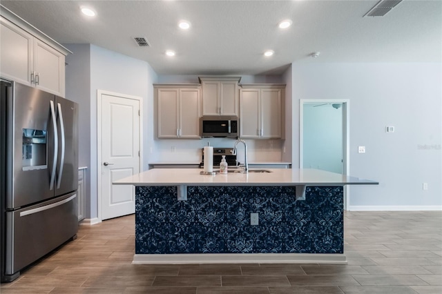 kitchen featuring a kitchen island with sink, sink, gray cabinets, light wood-type flooring, and stainless steel appliances