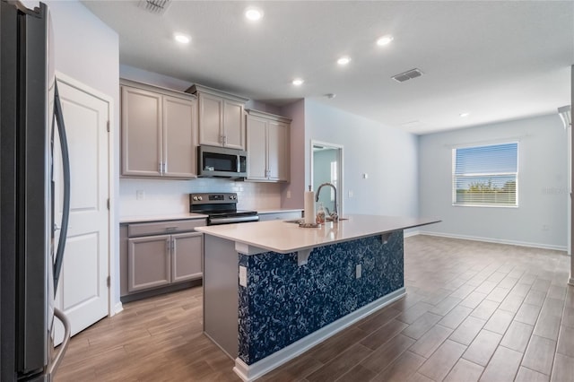 kitchen featuring gray cabinets, sink, an island with sink, and stainless steel appliances