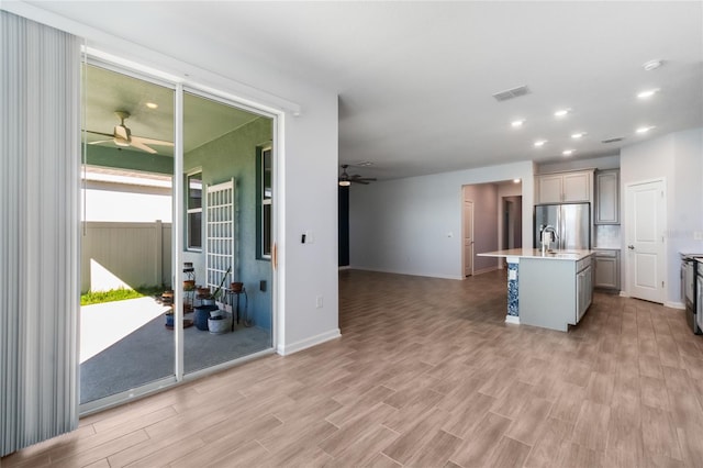 kitchen featuring light wood-type flooring, a center island with sink, stainless steel appliances, and ceiling fan