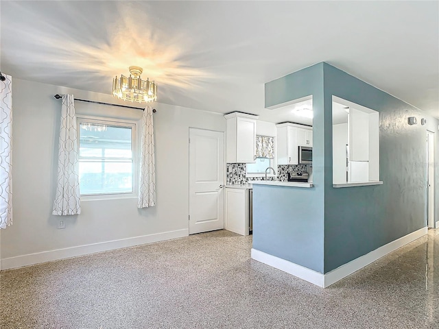 kitchen featuring backsplash, white cabinetry, sink, and a notable chandelier