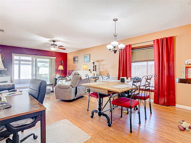 dining room with ceiling fan with notable chandelier, a textured ceiling, and light hardwood / wood-style flooring