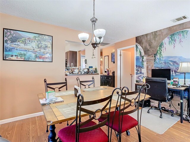 dining space featuring a textured ceiling, light hardwood / wood-style flooring, and an inviting chandelier