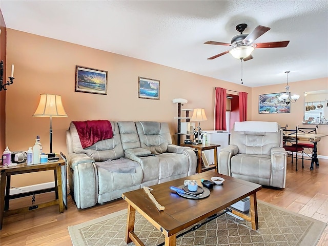 living room with ceiling fan with notable chandelier, light wood-type flooring, and a textured ceiling