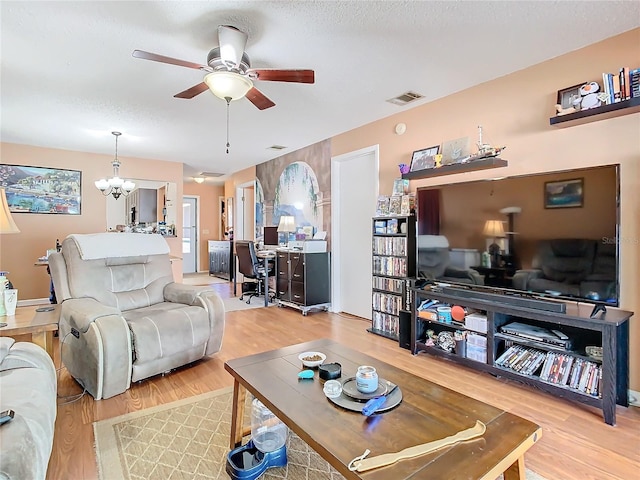 living room featuring ceiling fan with notable chandelier, light wood-type flooring, and a textured ceiling