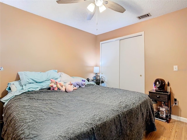 bedroom featuring a textured ceiling, a closet, light hardwood / wood-style flooring, and ceiling fan