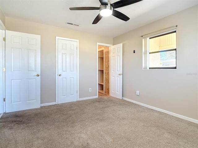 unfurnished bedroom with ceiling fan, a spacious closet, and light carpet