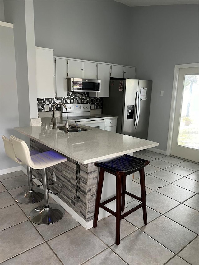 kitchen featuring sink, stainless steel appliances, kitchen peninsula, a towering ceiling, and a breakfast bar