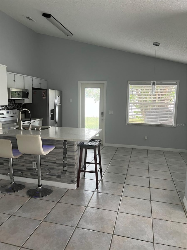 kitchen featuring a breakfast bar, white cabinets, hanging light fixtures, vaulted ceiling, and appliances with stainless steel finishes