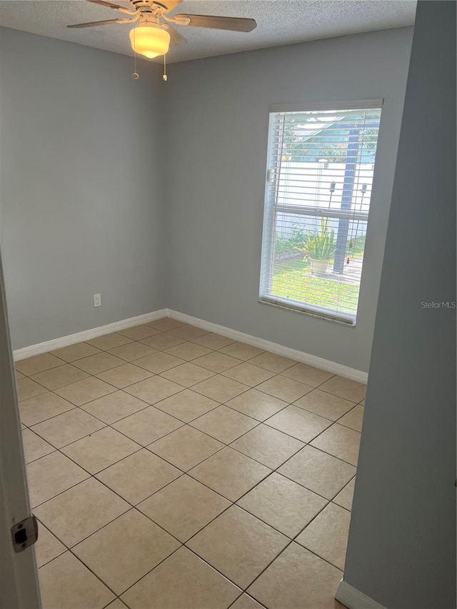 empty room featuring ceiling fan, light tile patterned flooring, and a textured ceiling