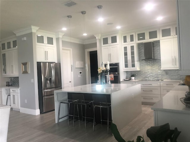 kitchen with white cabinets, appliances with stainless steel finishes, a center island, and wall chimney exhaust hood