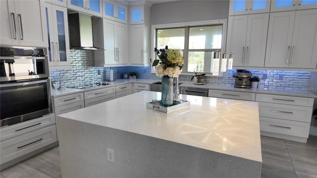 kitchen featuring a center island, white cabinets, wall chimney range hood, decorative backsplash, and stainless steel appliances