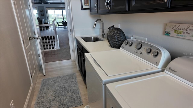 laundry area featuring cabinets, sink, washing machine and dryer, and light hardwood / wood-style flooring