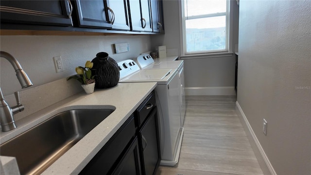 laundry room featuring cabinets, washing machine and dryer, light hardwood / wood-style floors, and sink