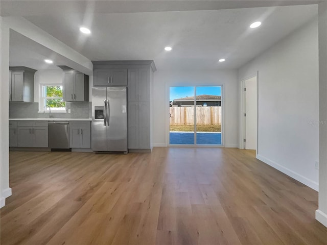 kitchen featuring decorative backsplash, appliances with stainless steel finishes, gray cabinetry, sink, and light hardwood / wood-style floors