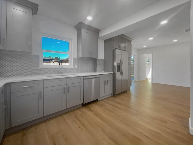 kitchen with decorative backsplash, gray cabinetry, stainless steel appliances, a healthy amount of sunlight, and light hardwood / wood-style flooring