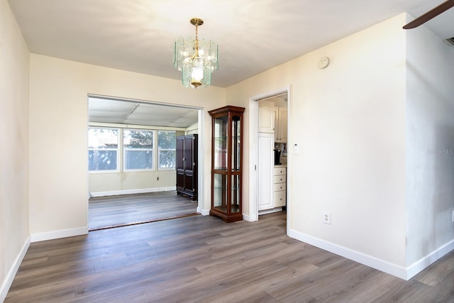 unfurnished dining area featuring a chandelier, baseboards, and wood finished floors