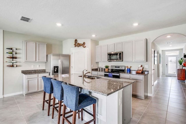 kitchen with sink, light stone counters, a textured ceiling, a kitchen island with sink, and appliances with stainless steel finishes