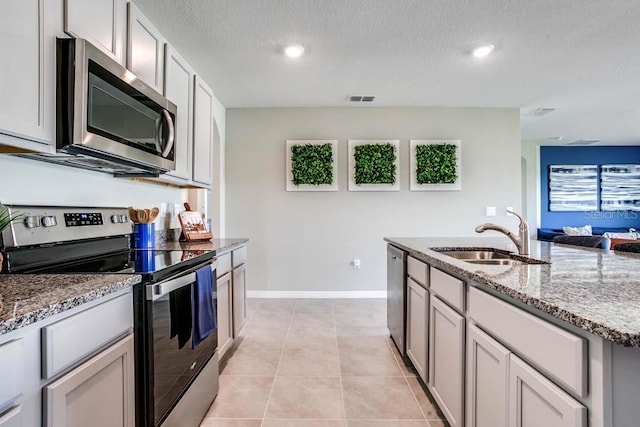 kitchen featuring sink, light tile patterned floors, a textured ceiling, light stone countertops, and appliances with stainless steel finishes