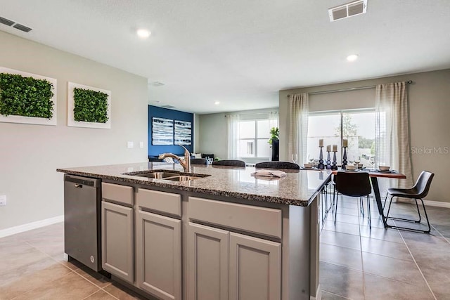 kitchen featuring dishwasher, a kitchen island with sink, sink, gray cabinets, and light stone countertops