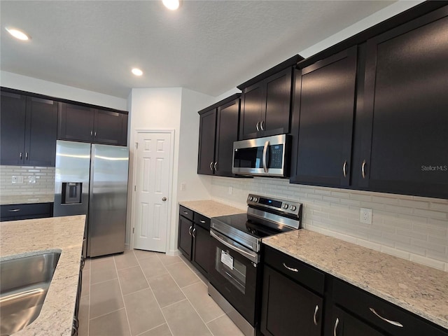 kitchen featuring decorative backsplash, sink, light stone countertops, stainless steel appliances, and light tile patterned floors