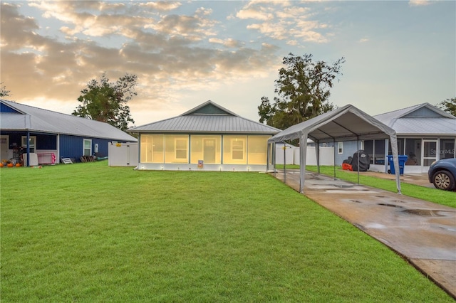 back house at dusk featuring a carport, a sunroom, and a yard