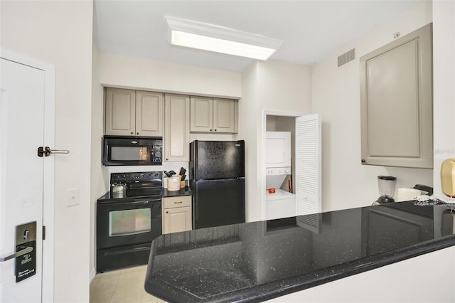 kitchen featuring stacked washer / dryer, kitchen peninsula, light tile patterned floors, and black appliances