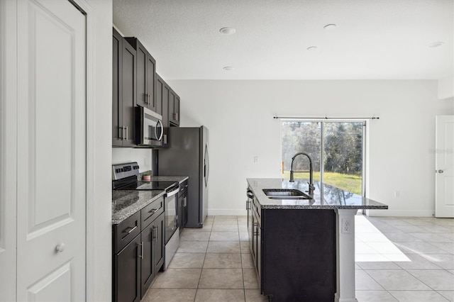 kitchen with appliances with stainless steel finishes, a kitchen island with sink, dark stone counters, and sink