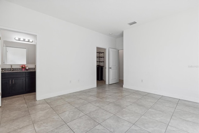 interior space with a spacious closet, sink, light tile patterned floors, and ensuite bathroom