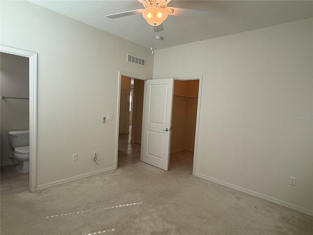 unfurnished bedroom with ceiling fan, light colored carpet, a spacious closet, and connected bathroom