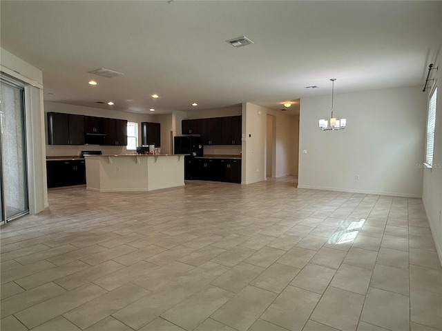 kitchen featuring refrigerator, ventilation hood, a notable chandelier, hanging light fixtures, and an island with sink