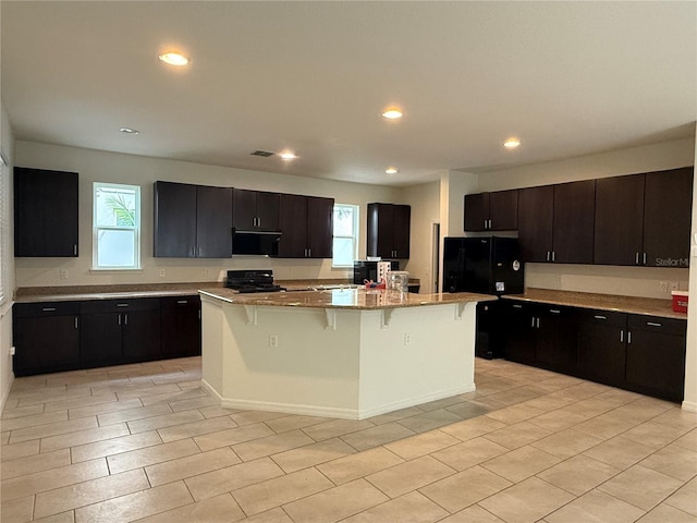 kitchen featuring black appliances, a kitchen breakfast bar, light stone countertops, a kitchen island, and dark brown cabinetry