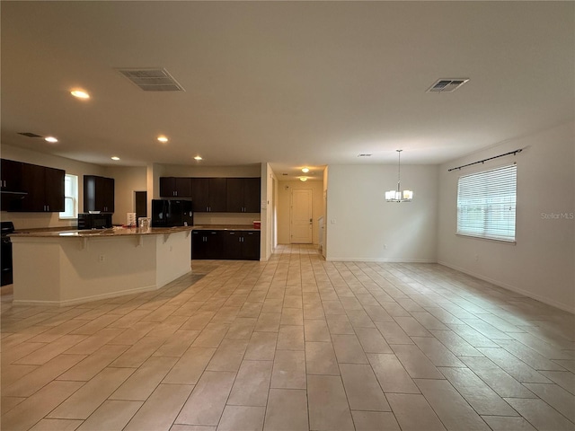 kitchen featuring dark brown cabinets, black appliances, a center island with sink, a chandelier, and a breakfast bar area