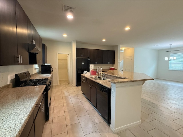 kitchen with light stone countertops, sink, an inviting chandelier, a kitchen island with sink, and black appliances