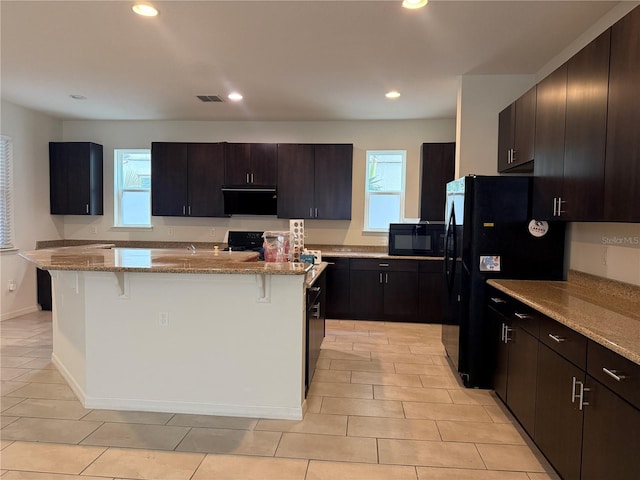 kitchen featuring black appliances, dark brown cabinets, a healthy amount of sunlight, and a kitchen bar