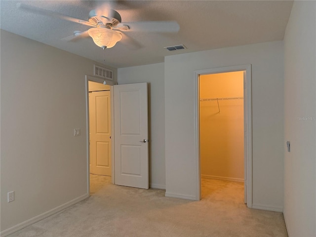 unfurnished bedroom featuring light carpet, a closet, a spacious closet, and ceiling fan