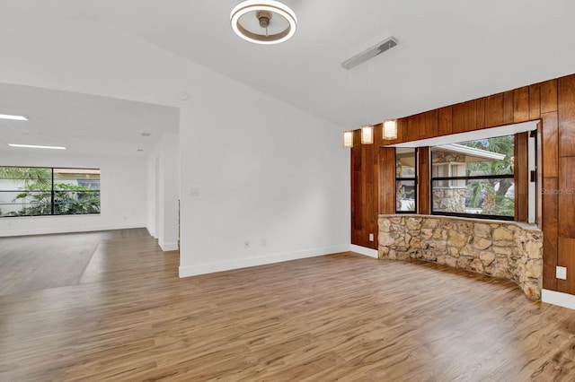 unfurnished living room featuring wooden walls, vaulted ceiling, a wealth of natural light, and light hardwood / wood-style flooring