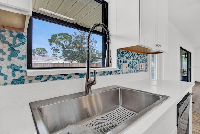 room details featuring white cabinets, black dishwasher, sink, and tasteful backsplash