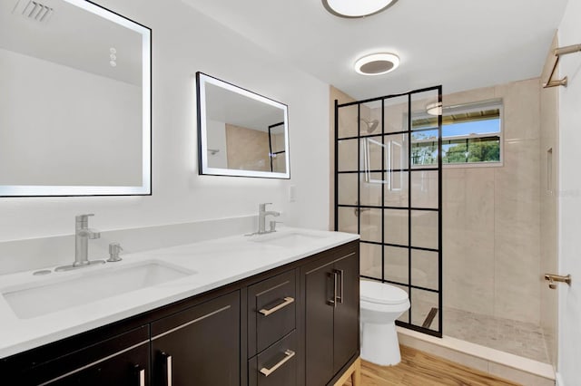 bathroom with vanity, toilet, a tile shower, and wood-type flooring