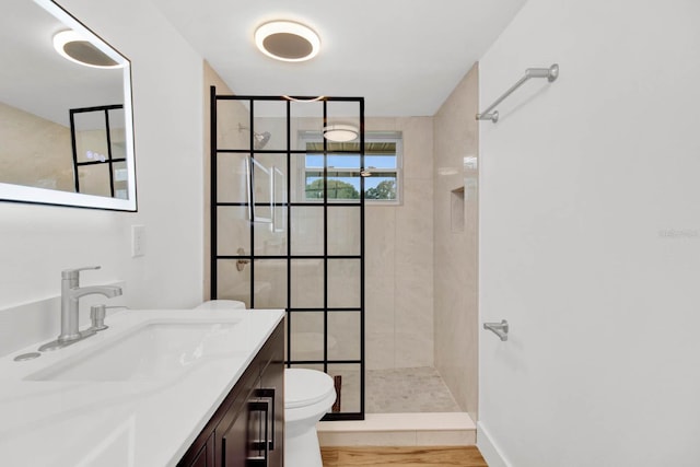 bathroom featuring a tile shower, toilet, vanity, and hardwood / wood-style flooring