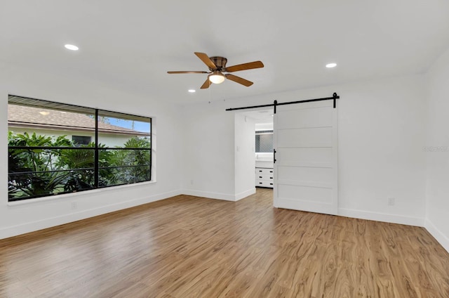 empty room with a barn door, ceiling fan, and light hardwood / wood-style flooring