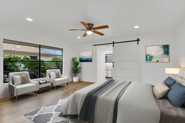 bedroom featuring a barn door, hardwood / wood-style flooring, ensuite bath, and ceiling fan