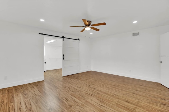 empty room featuring ceiling fan, a barn door, and light hardwood / wood-style floors