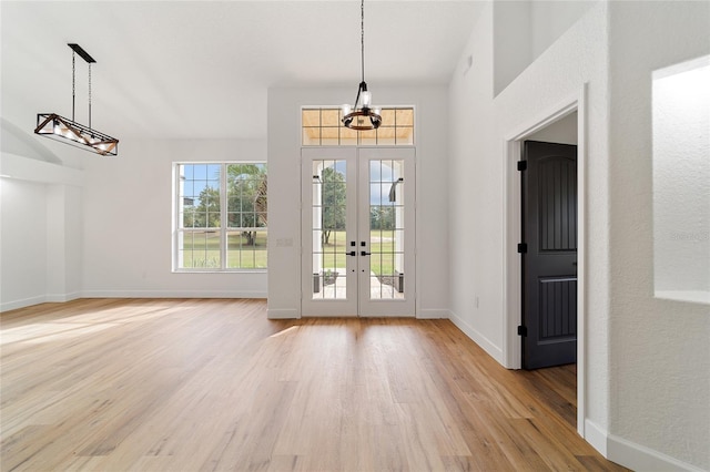 entryway with french doors, a towering ceiling, light hardwood / wood-style flooring, and a notable chandelier