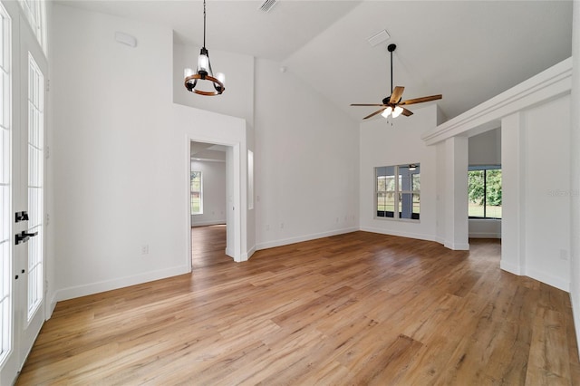 unfurnished living room featuring plenty of natural light, light hardwood / wood-style floors, ceiling fan with notable chandelier, and high vaulted ceiling