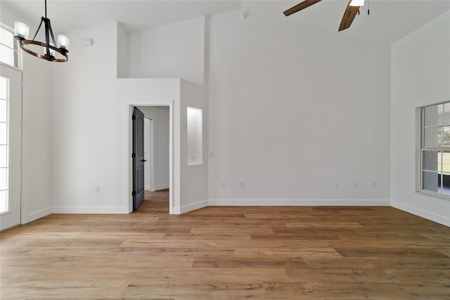 spare room with ceiling fan with notable chandelier, light wood-type flooring, and high vaulted ceiling