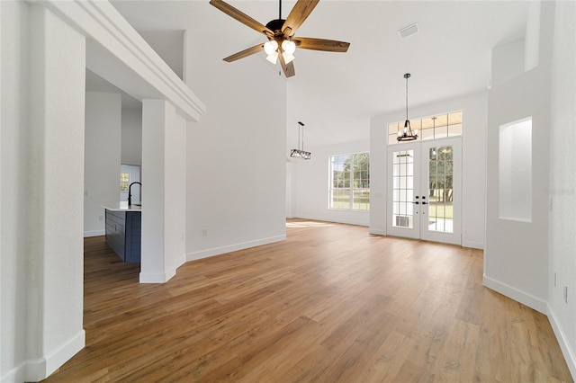 unfurnished living room with french doors, sink, ceiling fan, light wood-type flooring, and a towering ceiling