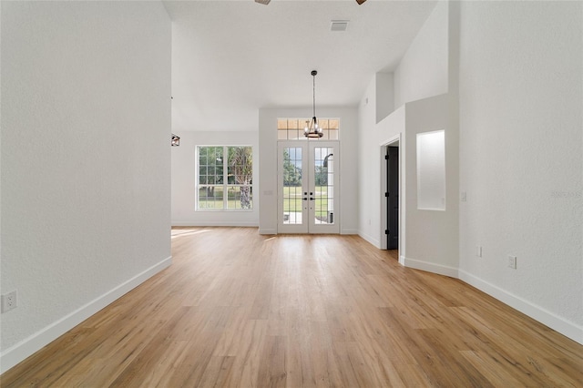 unfurnished living room with french doors, a high ceiling, a notable chandelier, and light wood-type flooring