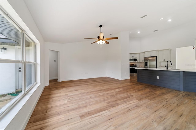 unfurnished living room featuring light hardwood / wood-style floors, ceiling fan, and sink