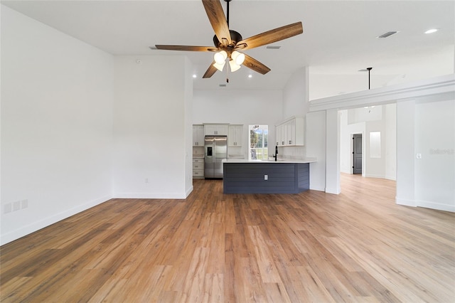 unfurnished living room with ceiling fan, light hardwood / wood-style flooring, high vaulted ceiling, and sink